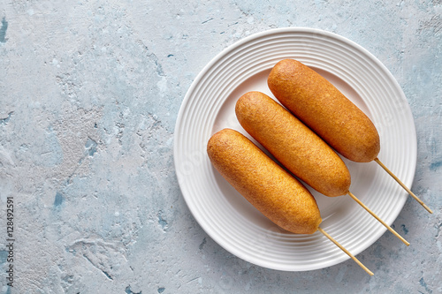 Corn dog traditional American corndog street food deep fried hotdog meat sausage snack treat coated in a thick layer of cornmeal batter on stick unhealthy eating on rustic table.