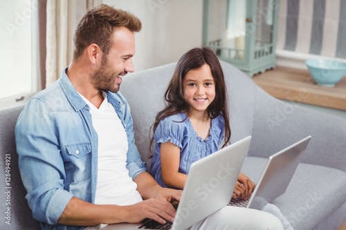 Happy father and daughter using laptop on sofa