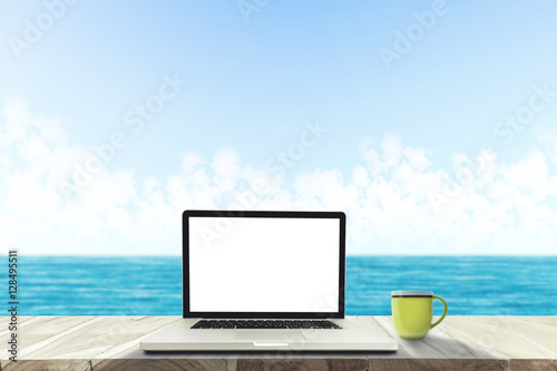 A laptop and a coffee cup on wood table in the sea beach . © Jettana