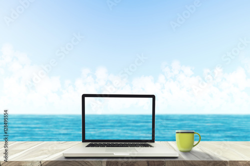 A laptop and a coffee cup on wood table in the sea beach . © Jettana