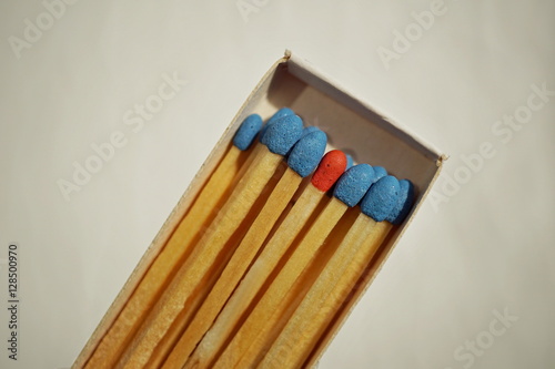 Macro detail of a box of matches (matchbox) full of matches with blue top and one different with a red top as a symbol of difference, differentness and dissimilarity 