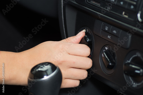 Closeup inside vehicle of hand twisting instrument on dashboard, black interior background, female driver concept © Fotos 593