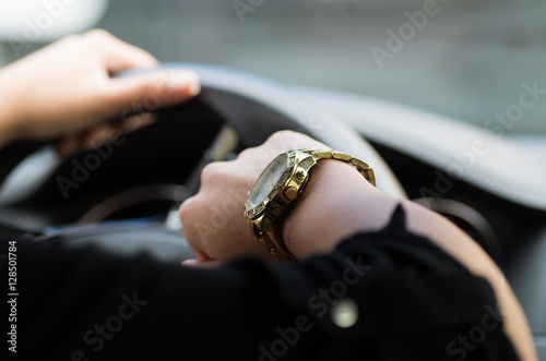 Closeup inside vehicle of woman s hand holding onto steering wheel  other arm showing off wrist watch  female driver concept