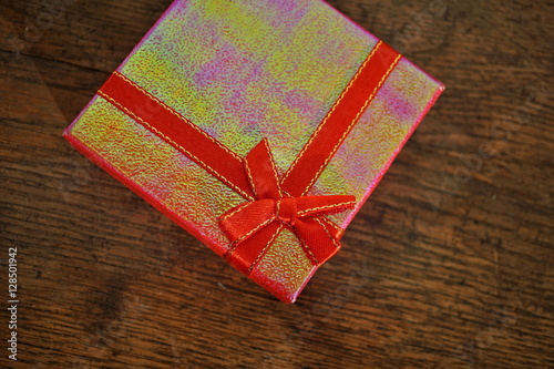 Top view of a glittering present with red ribbon and golden stitching on the vintaged wooden background 