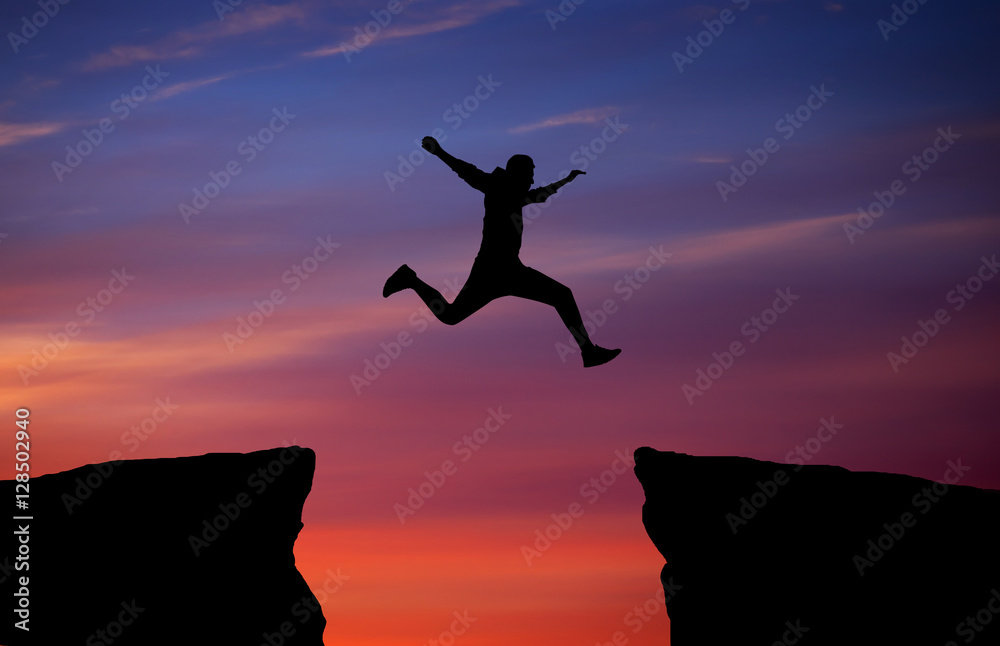 Man jumping across the gap from one rock to cling to the other.