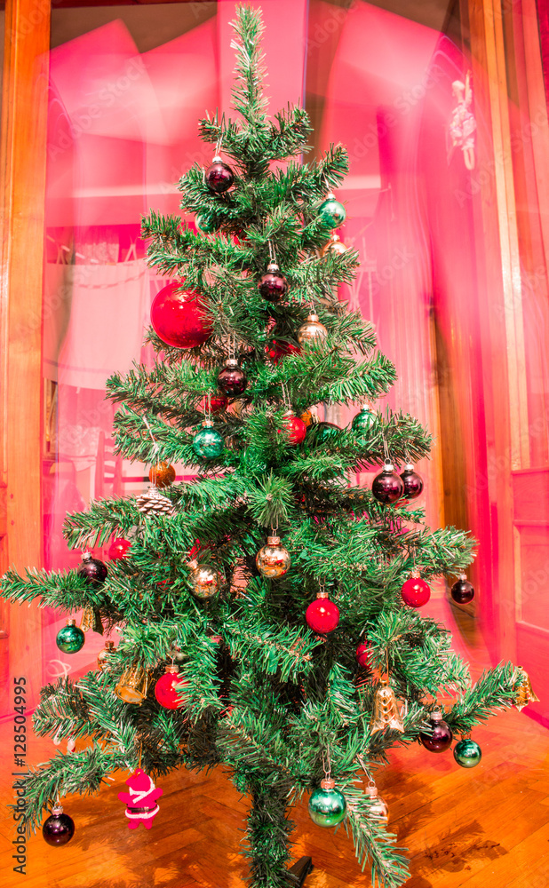 Artificial Christmas tree with colorful ornaments on red background 