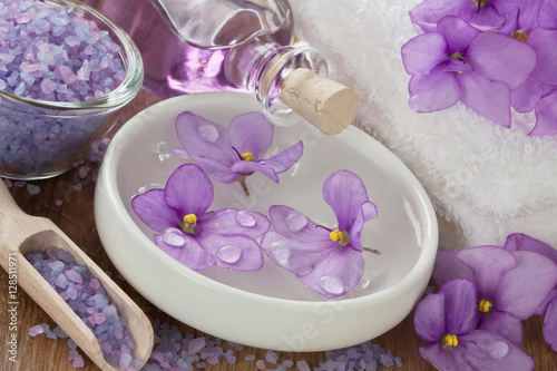 SPA treatment set   Floating violet flower in water  aromatic essential oil  sea salt  soft towel and on wooden background