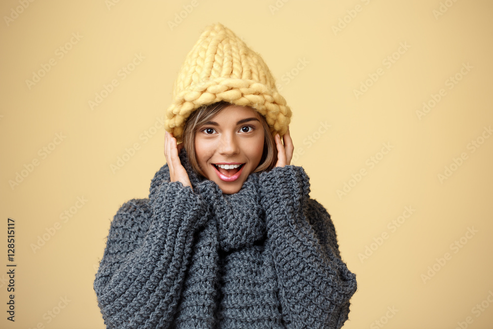 Young beautiful fair-haired girl in knited hat and sweater smiling looking at camera over yellow background. Young beautiful fair-haired girl in knited hat and sweater smiling looking at camera over yellow background.