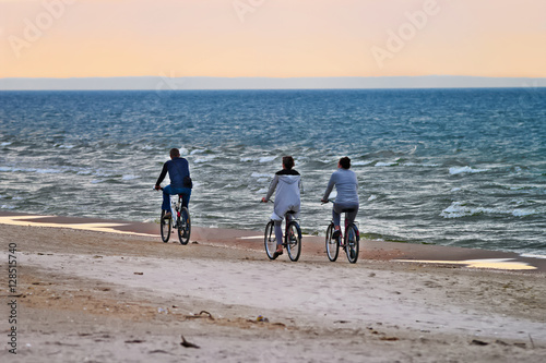Group of cyclists on the beach riding bicycles along the seaside in the evening. Selective focus.  Stegna, Pomerania, northern Poland.