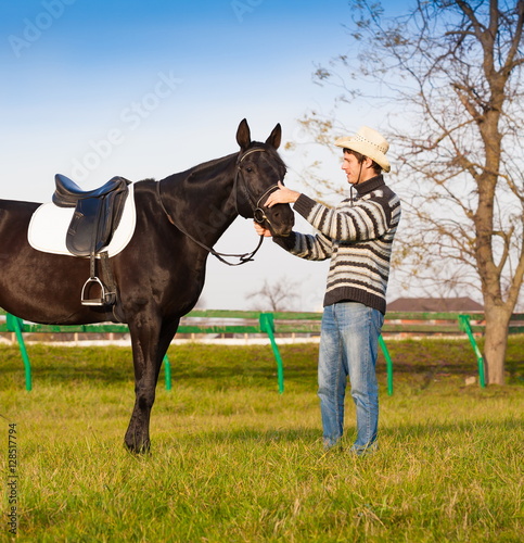 Man nearby horse, striped pullover, blue jeans, hat, landscape