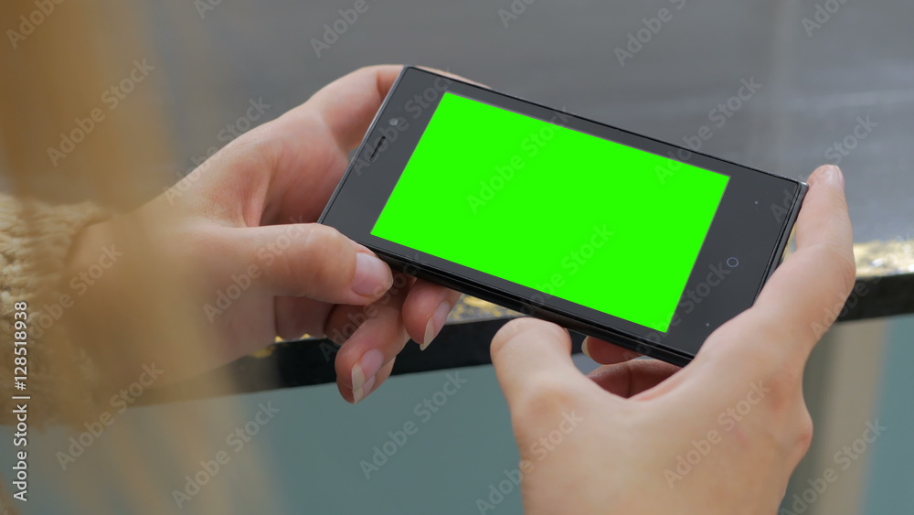 Woman looking at horizontal smartphone with green screen. Close up shot of woman's hands with mobile Woman looking at horizontal smartphone with green screen. Close up shot of woman's hands with mobile