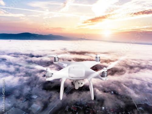 Hovering drone taking pictures of town covered by mist, sunrise © Halfpoint