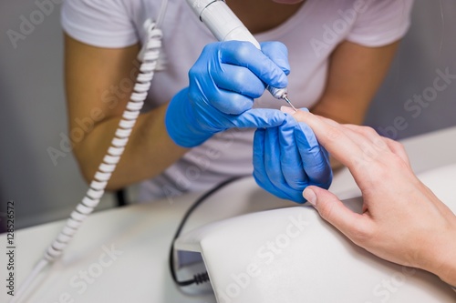 Closeup shot of a woman in a nail salon receiving a manicure by a beautician with electric nail file. Woman getting nail manicure. Beautician file nails to a customer
