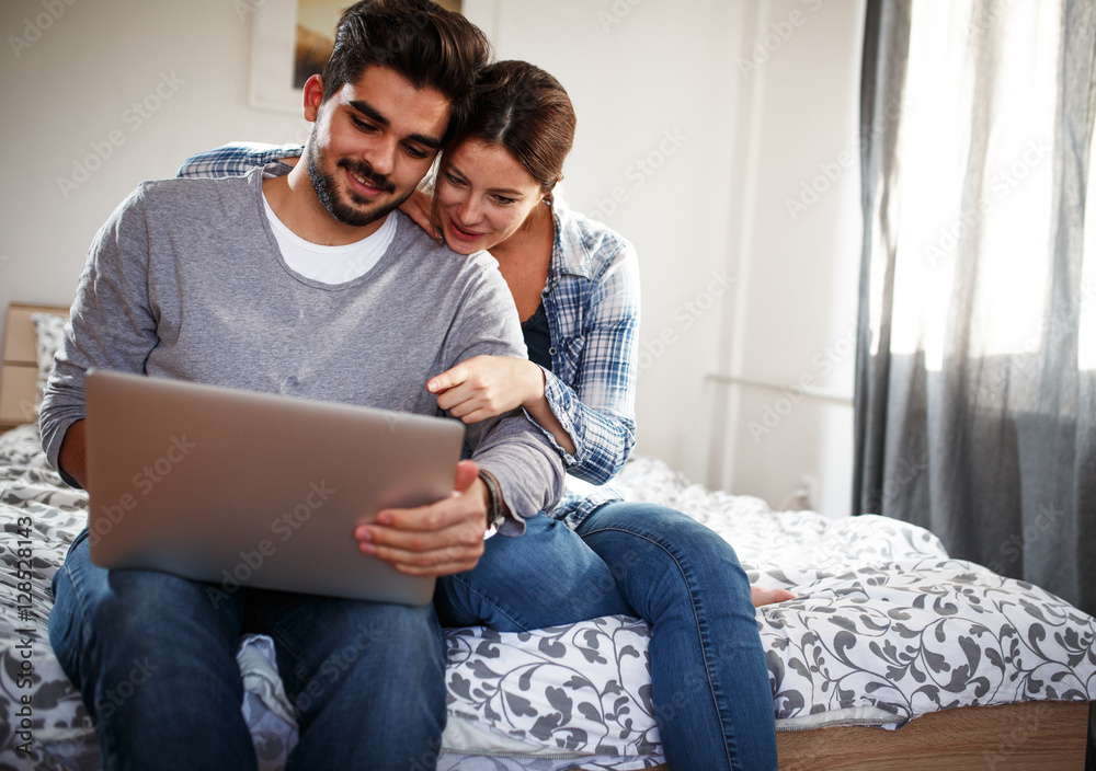 Young married couple sitting on bed at home and using laptop.