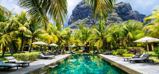 High resolution panorama of Le Morne Brabant mountain overlooking a luxury resort infinity pool. Exclusive five-star hotel with palm trees and sunbeds in Mauritius.