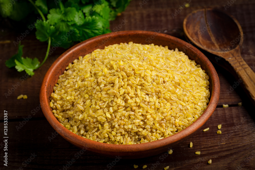 Raw bulgur, wheat grains in bowl on wooden table. Close up view Raw bulgur, wheat grains in bowl on wooden table. Close up view