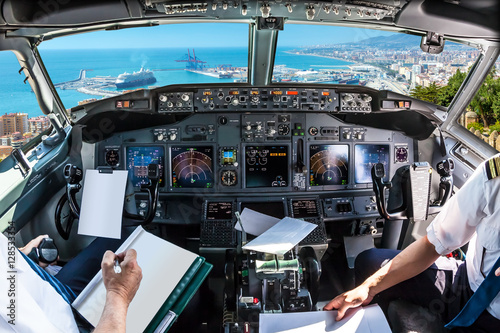 Airplane cockpit flying on port of Malaga from the Gibralfaro Castle, Andalusia, Spain, with pilots arms and blank white papers for copy space.