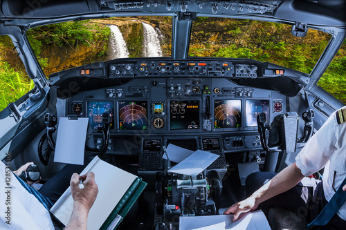 Airplane cockpit flying on ropical Manawaiopuna Falls also called Jurassic Park Falls, Kauai, Hawaii, United States, with pilots arms and blank white papers for copy space.
