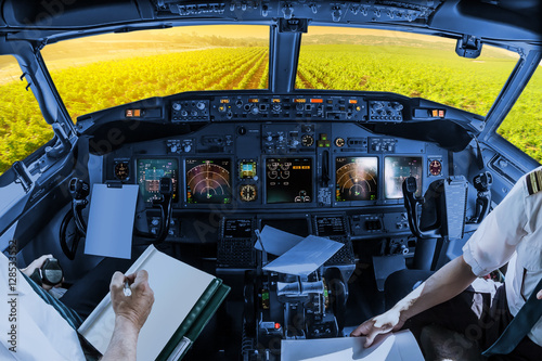 Fototapeta Naklejka Na Ścianę i Meble -  Airplane cockpit flying on Napa Valley at sunset, California, United States, with pilots arms and blank white papers for copy space.