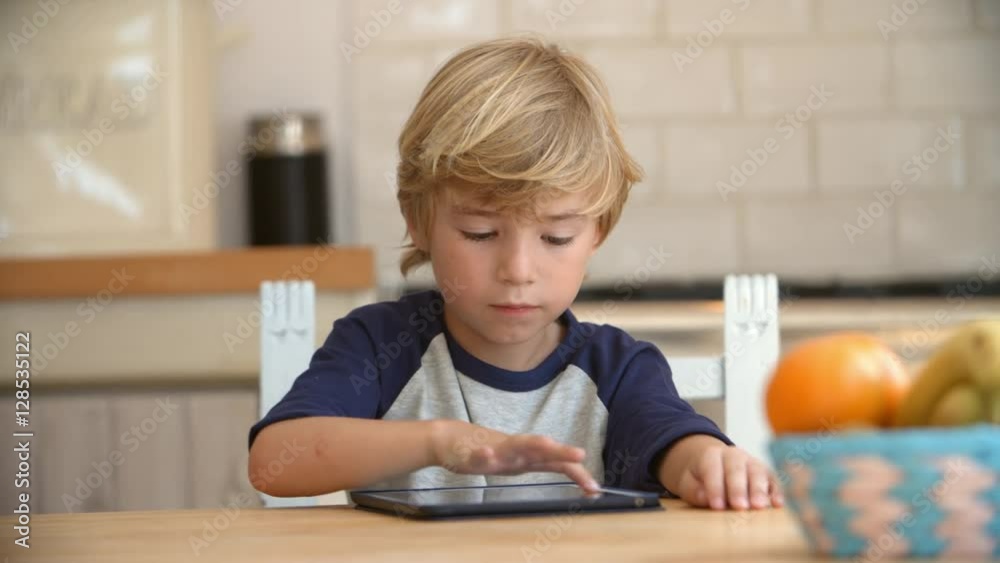 Young boy using tablet computer at kitchen table, pan Young boy using tablet computer at kitchen table, pan