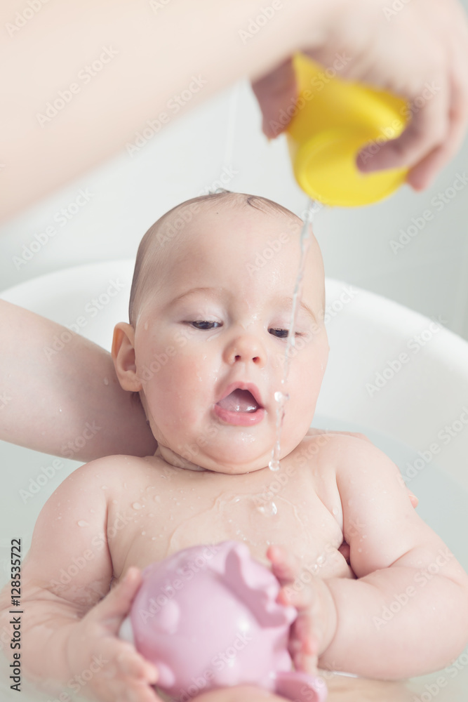 Seven months old baby girl in a bath, playing with pink toy and Stock