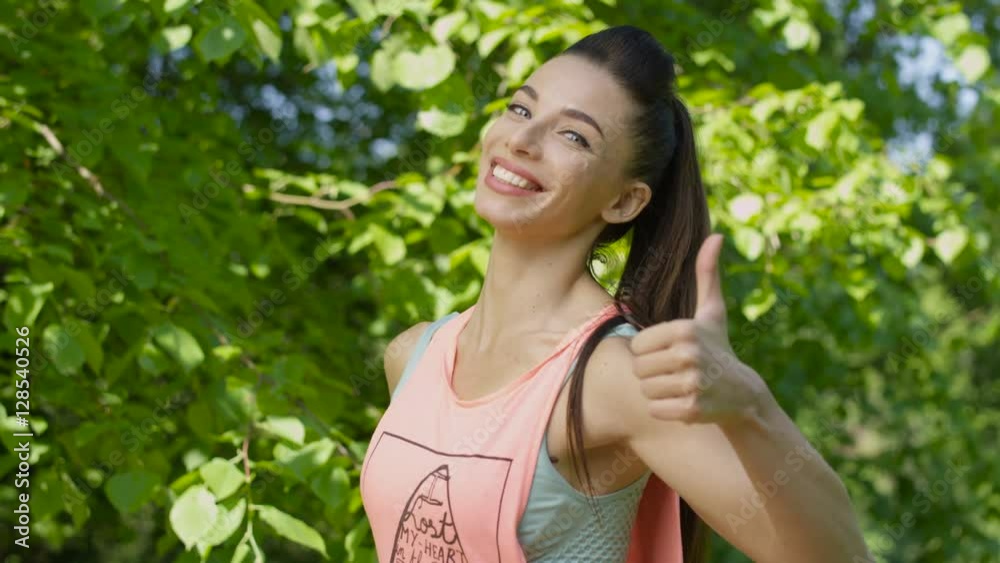 Fitness and lifestyle - portrait of a beautiful young woman after training in the park. Pretty young girl showing ok sign with thumb up and smiling to a camera. Fitness and lifestyle - portrait of a beautiful young woman after training in the park. Pretty young girl showing ok sign with thumb up and smiling to a camera.