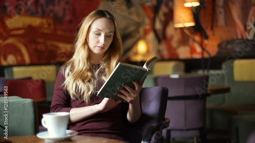 Pretty, blonde girl reading book and drinking coffee in the cafe
