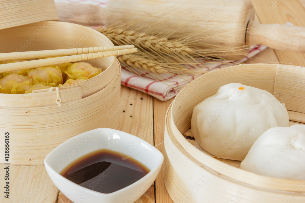 Steamed pork buns and chinese dim sum in bamboo basket, serve with chopsticks and napkin on wooden table background. Closed up