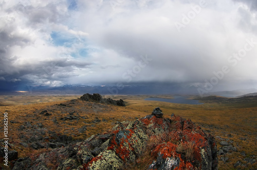Colorful rock in the background of valley with highland steppe lake with snow covered mountains under a stormy cloudy dramatic rain sky Plateau Ukok, Altai, Siberia, Russia