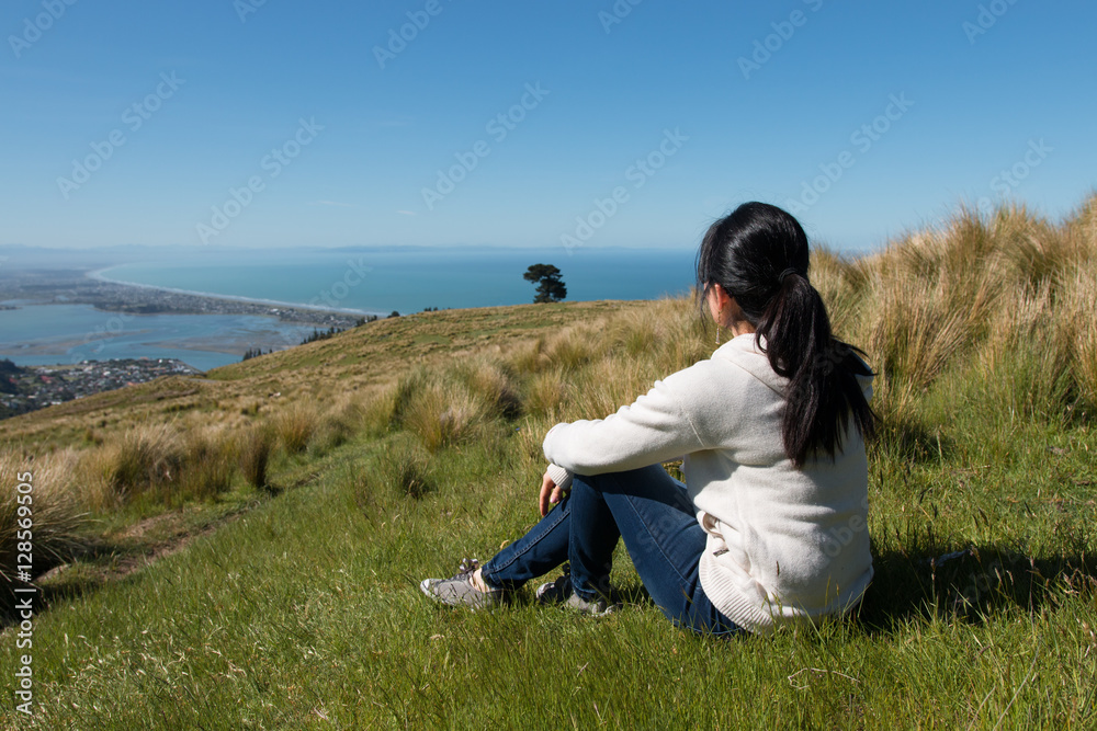Girl sits on hill top and looks at city below Girl sits on hill top and looks at city below