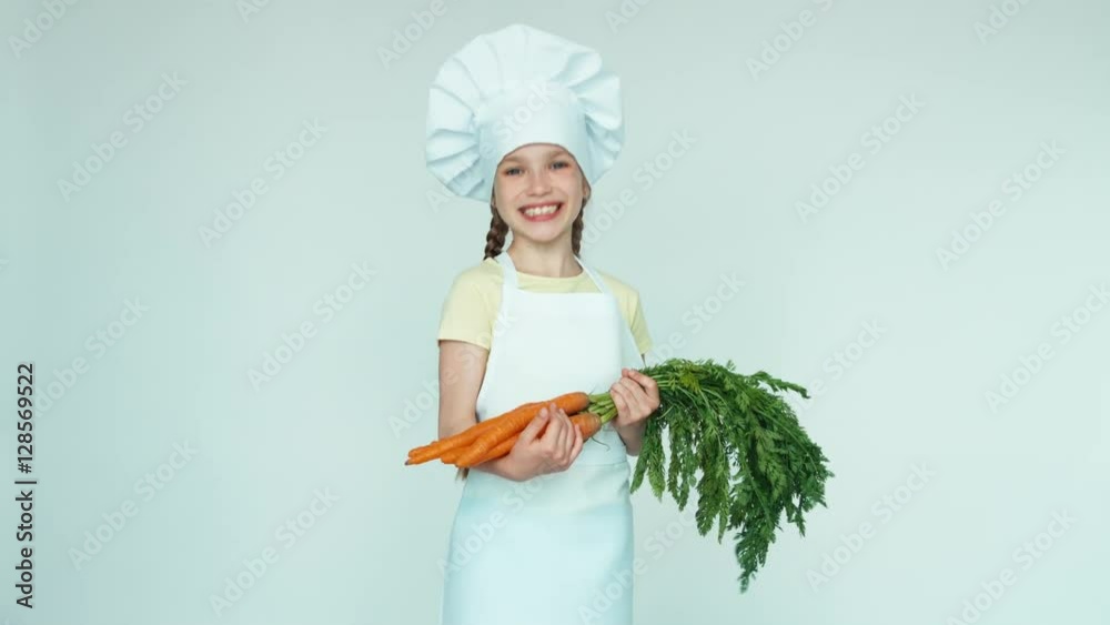 Portrait young chef girl holding carrots. Thumb up. Ok. Child 7-8 years old standing on white background Portrait young chef girl holding carrots. Thumb up. Ok. Child 7-8 years old standing on white background