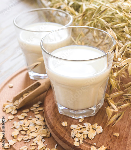 Two glasses of milk and oat spikelets on rustic table