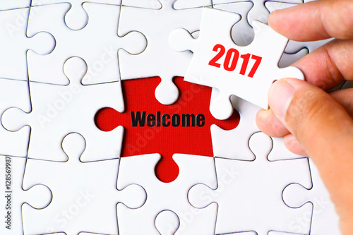 "Welcome" word on missing puzzle with a hand hold a piece of "2017" word puzzle want to complete it - business and finance concept