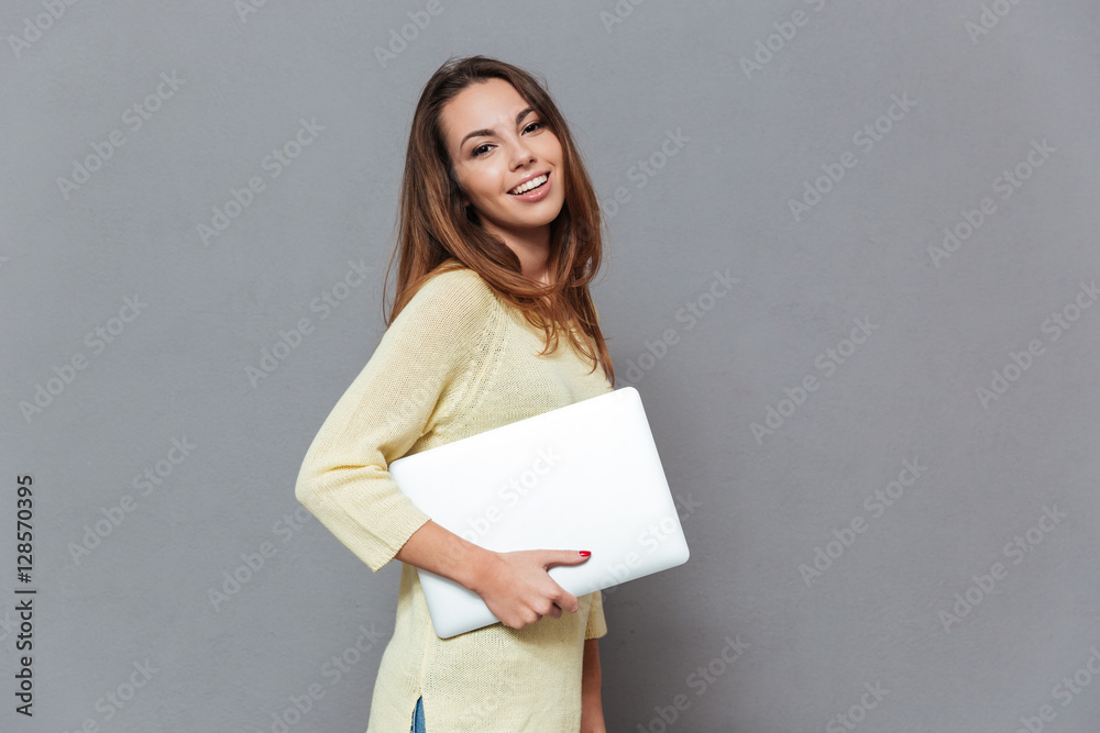 Portrait of a smiling brunette woman standing and holding laptop Portrait of a smiling brunette woman standing and holding laptop