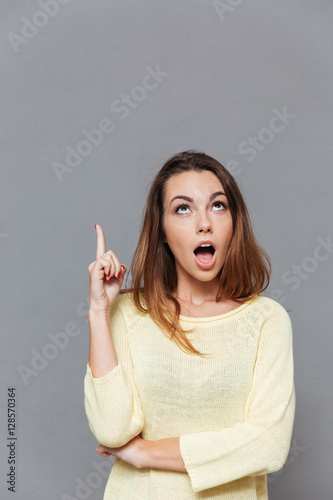 Amazed excited woman pointing finger up at copyspace