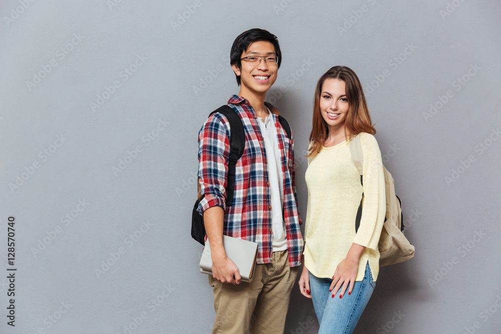 Cheerful student couple with backpacks and books looking at camera Cheerful student couple with backpacks and books looking at camera