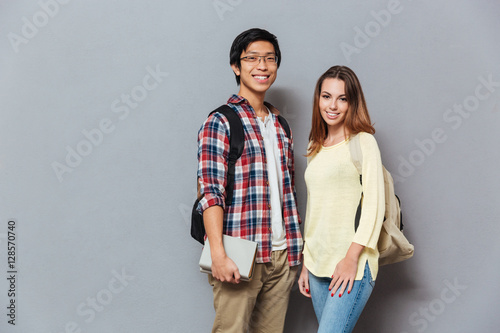 Cheerful student couple with backpacks and books looking at camera