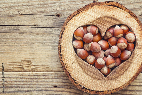 Hazelnut in a carved wooden heart on old wooden background. Top