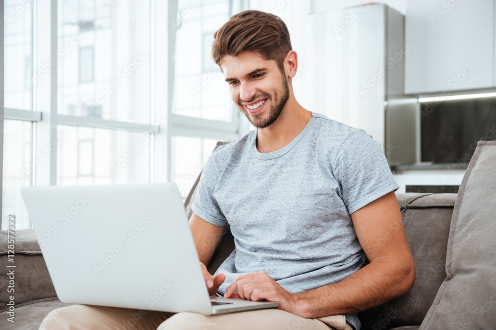 Happy young man sitting on sofa at home with laptop