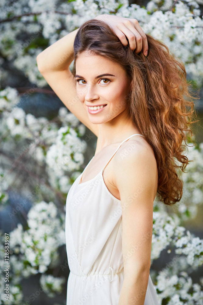 Naklejka premium Young beautiful woman in white dress enjoying of blooming tree