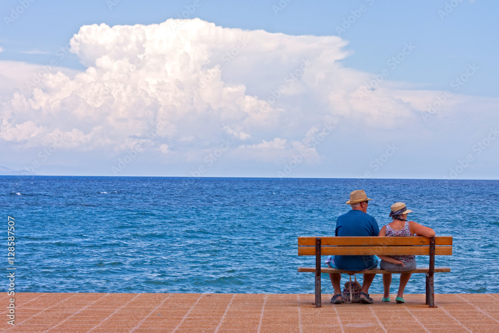 A copy of seniors sitting on a bench at sea shore