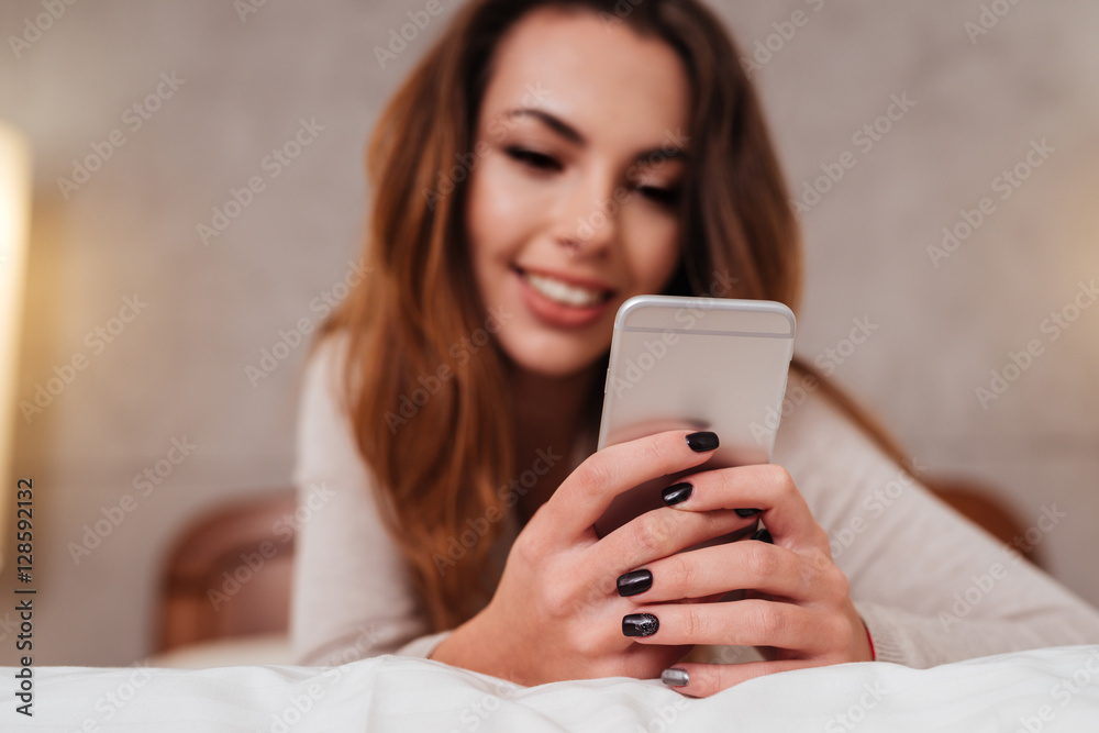 Woman using mobile phone while lying in bed at home Woman using mobile phone while lying in bed at home