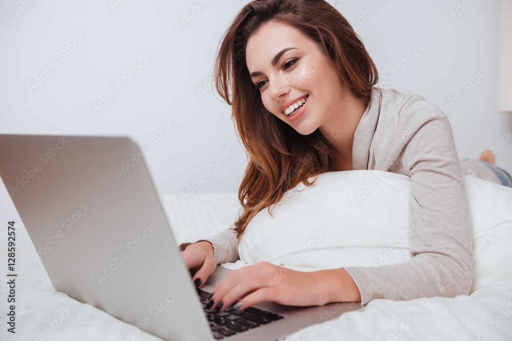 Cheerful smiling woman lying on bed and using laptop Cheerful smiling woman lying on bed and using laptop