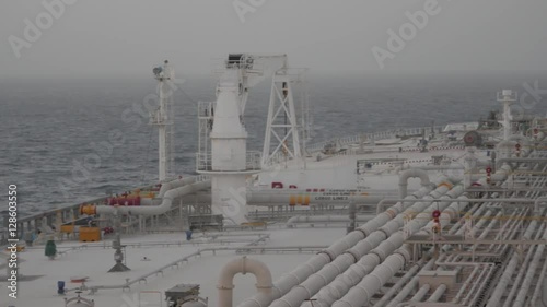 Deck of very large tanker, seaman walks, haze in Persian gulf.