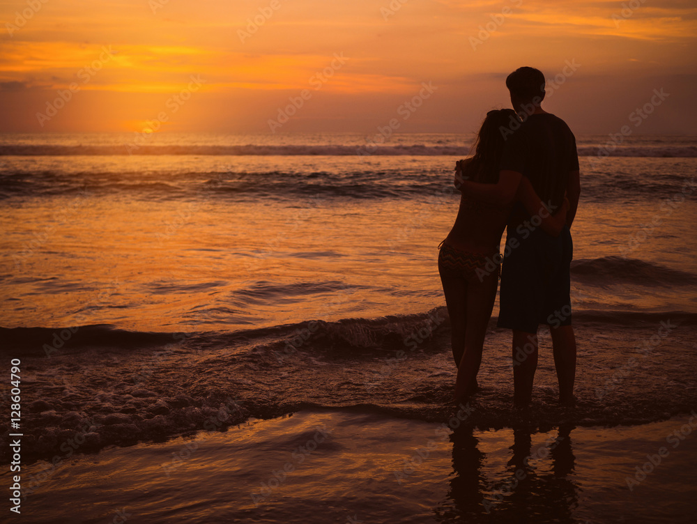 Beautiful young couple on sunset. Attractive people at sea, on background of bright orange sky and sea