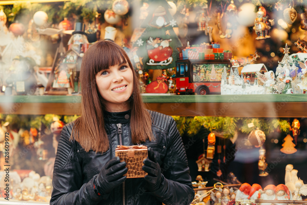 beautiful woman holding christmas present in front of christmas toys shop