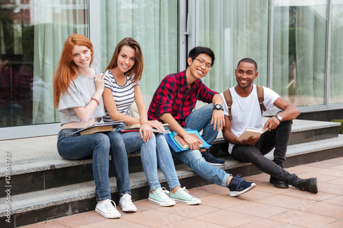 Cheerful young students sitting on stairs outdoors