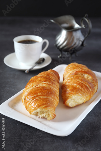 Two fresh croissants and cup of coffee on dark background