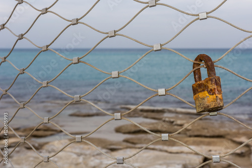 Single rusty Love Padlock on a fence along the coastline