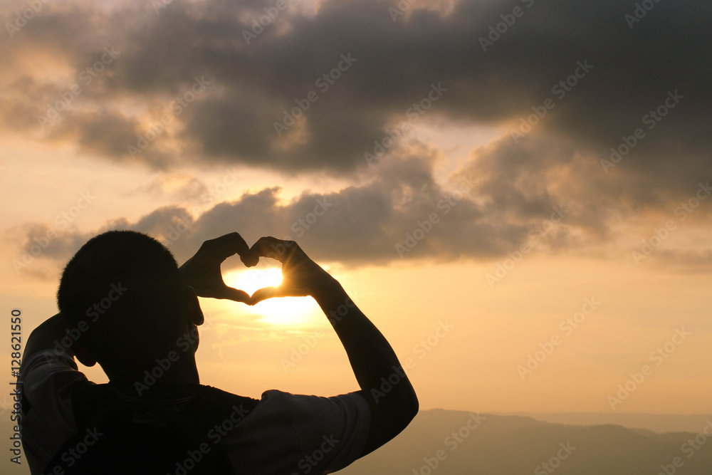 man  hands in the form of heart against the sky pass sun beams.